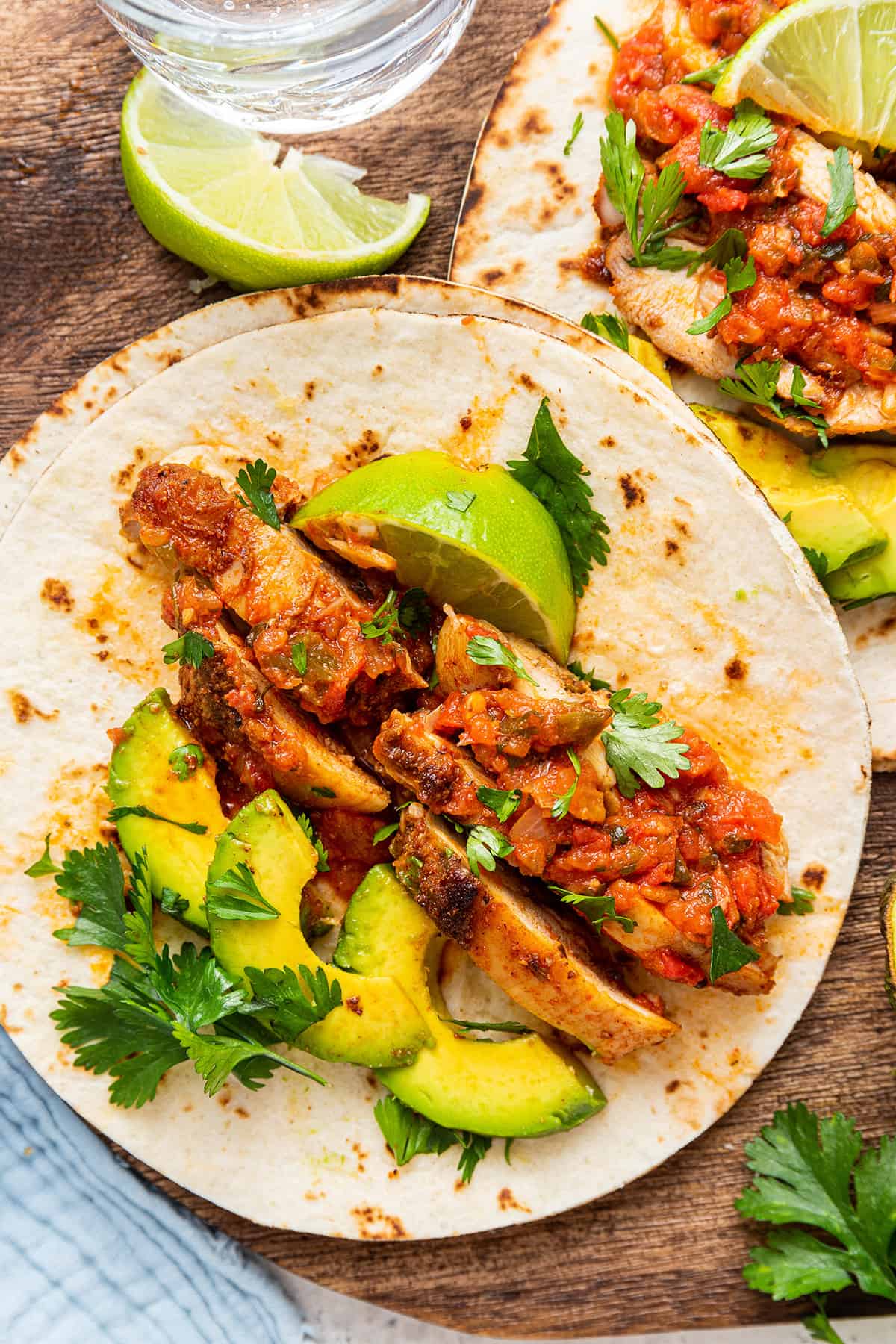 Overhead view of blackened chicken tacos on wood board, topped with avocado slices, cilantro, and lime wedge