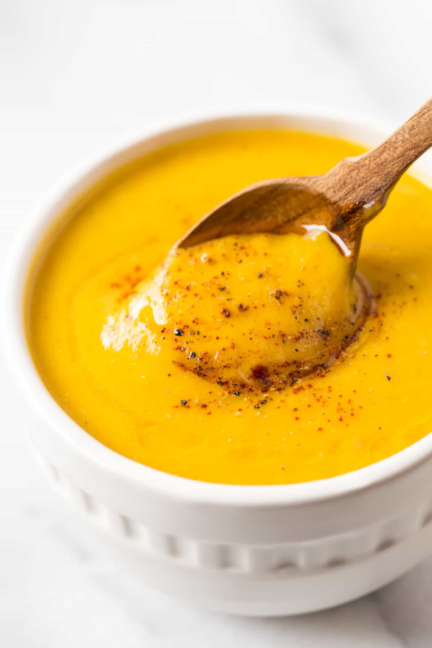 A spoon dipping into a bowl of squash soup topped with pepper and olive oil