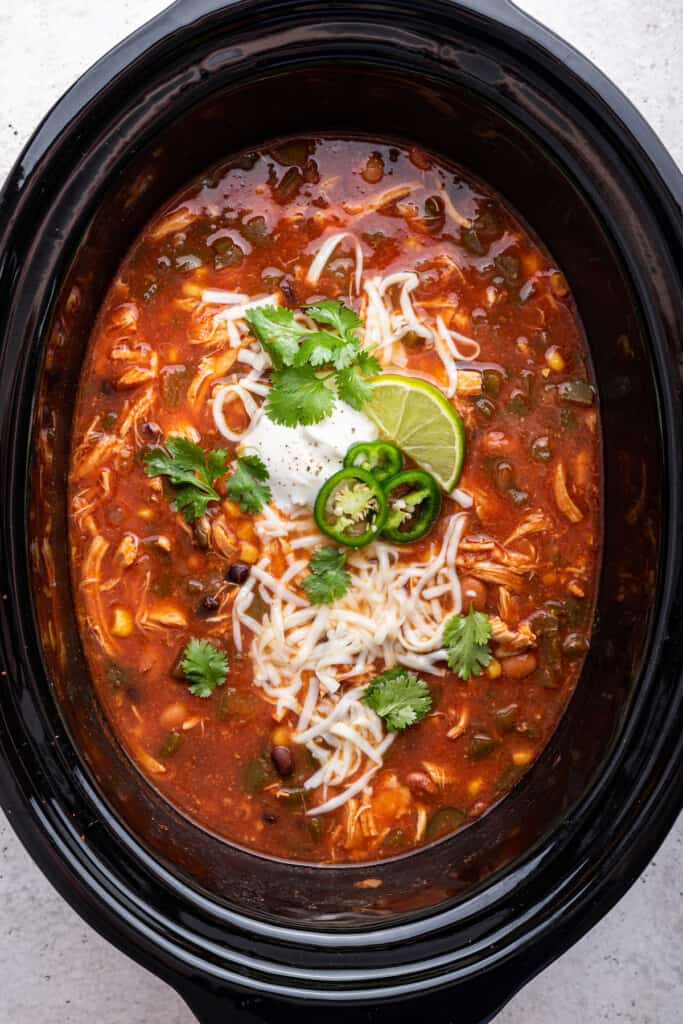 Overhead view of chicken taco soup in slow cooker with garnishes