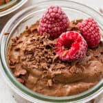 Close up of a jar of chocolate avocado mousse topped with raspberries