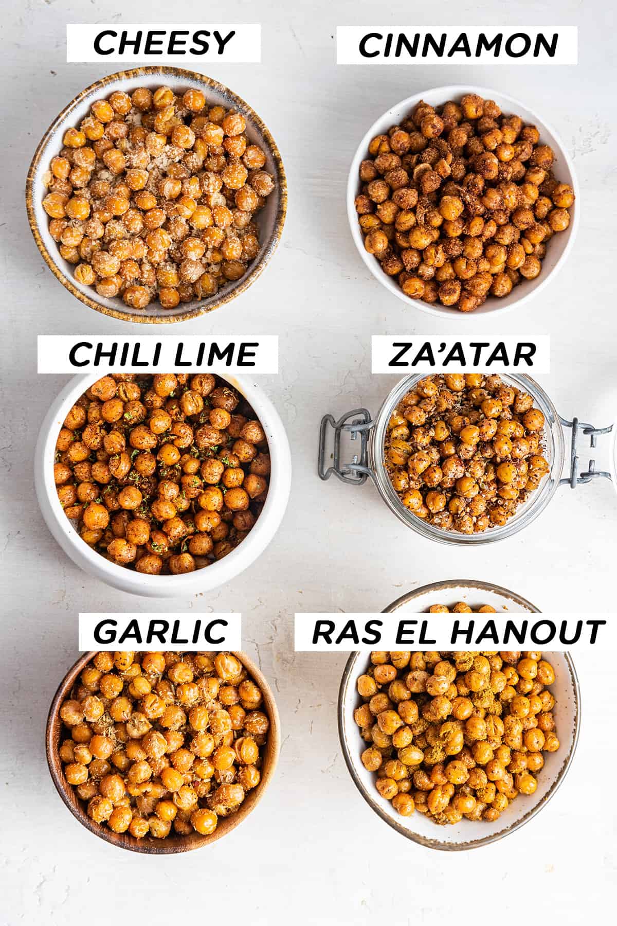 Overhead view of 6 bowls of crispy chickpeas, labeled: Cheesy, Cinnamon, Chili Lime, Za'Atar, Garlic, Ras el Hanout.