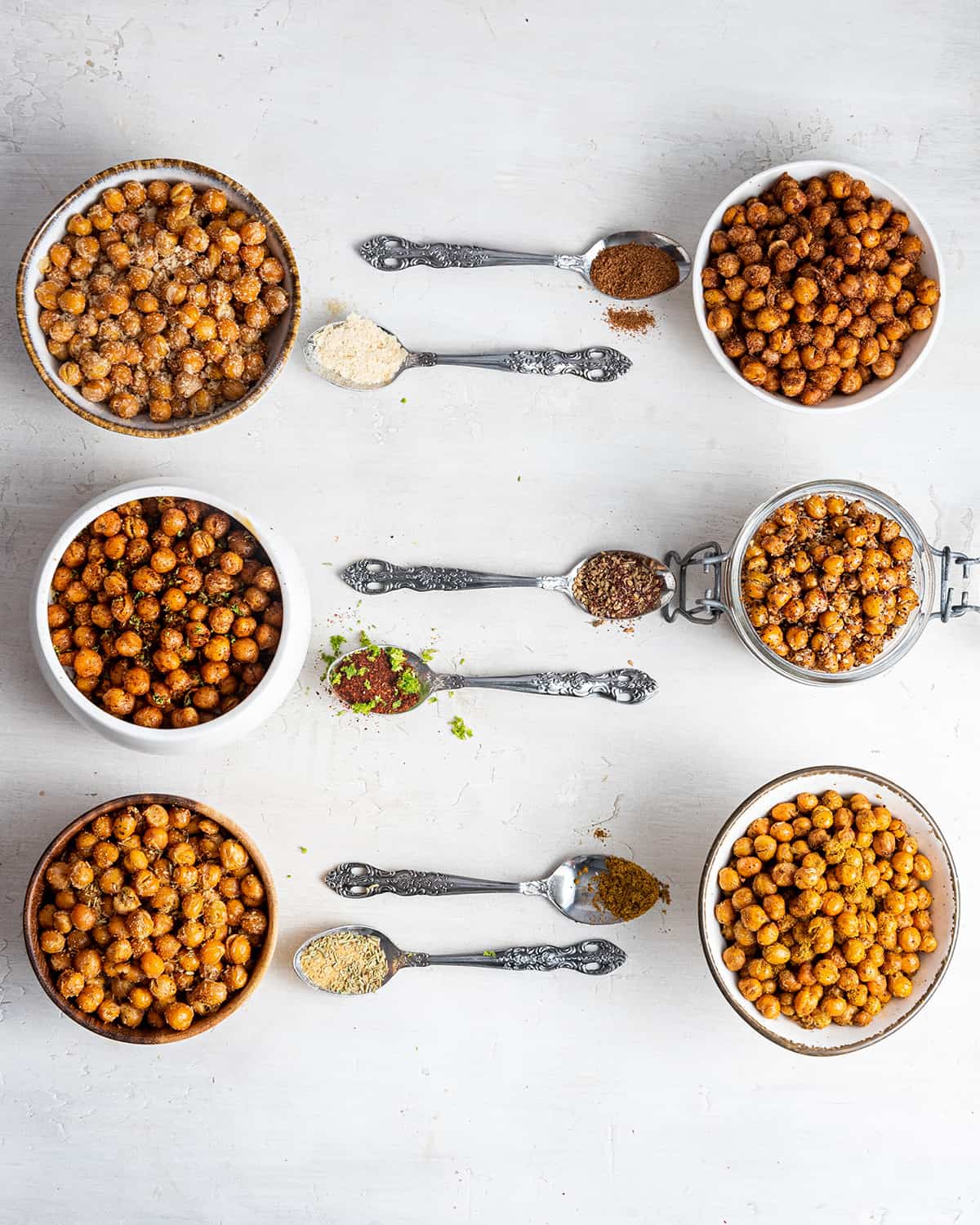 Six jars filled with crispy chickpeas, with a spoon in front of each
