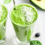 Angled top-down view of green smoothie in glass with stainless steel straw and shredded coconut garnish