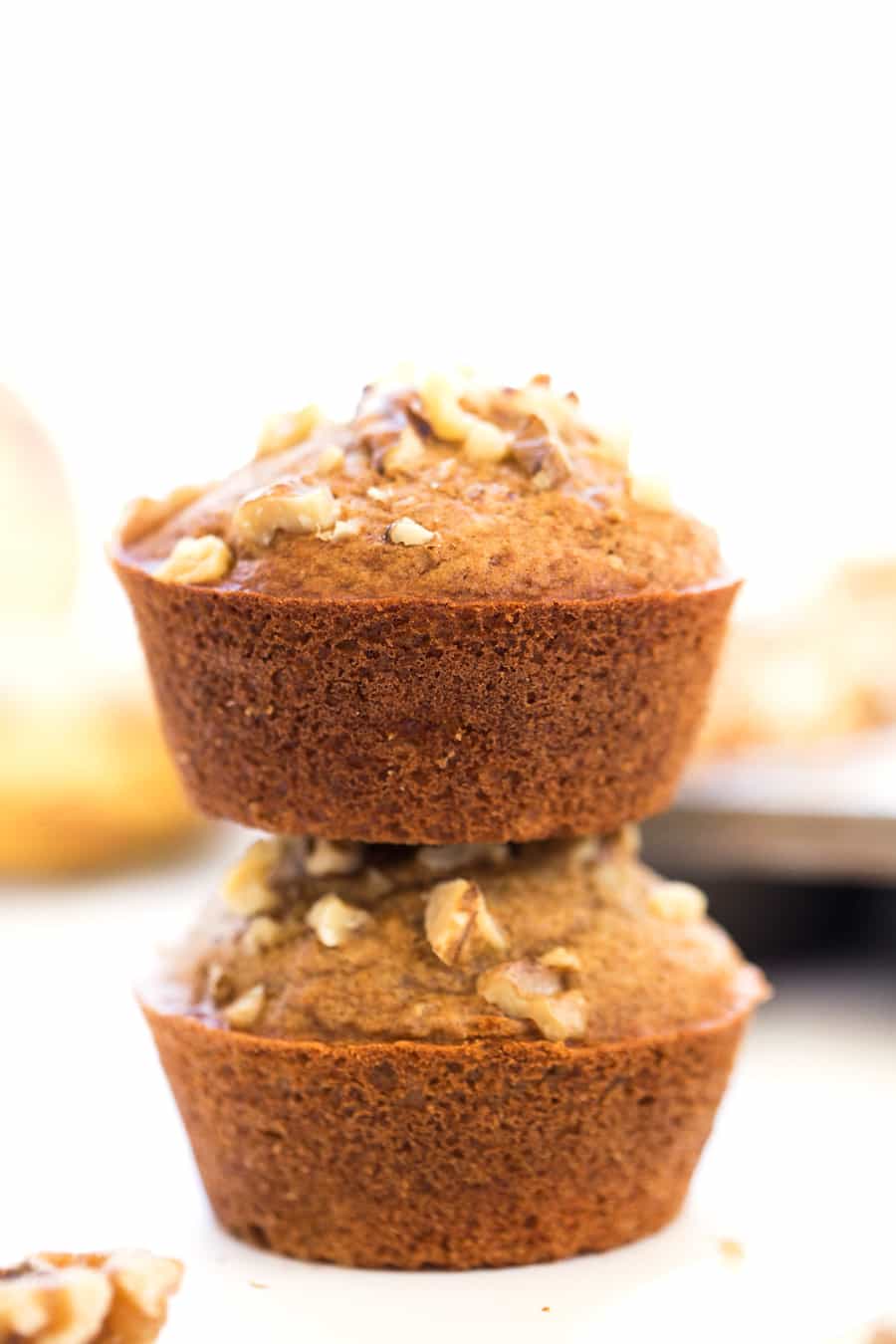 Two banana muffins topped with walnuts, stacked on top of each other. 