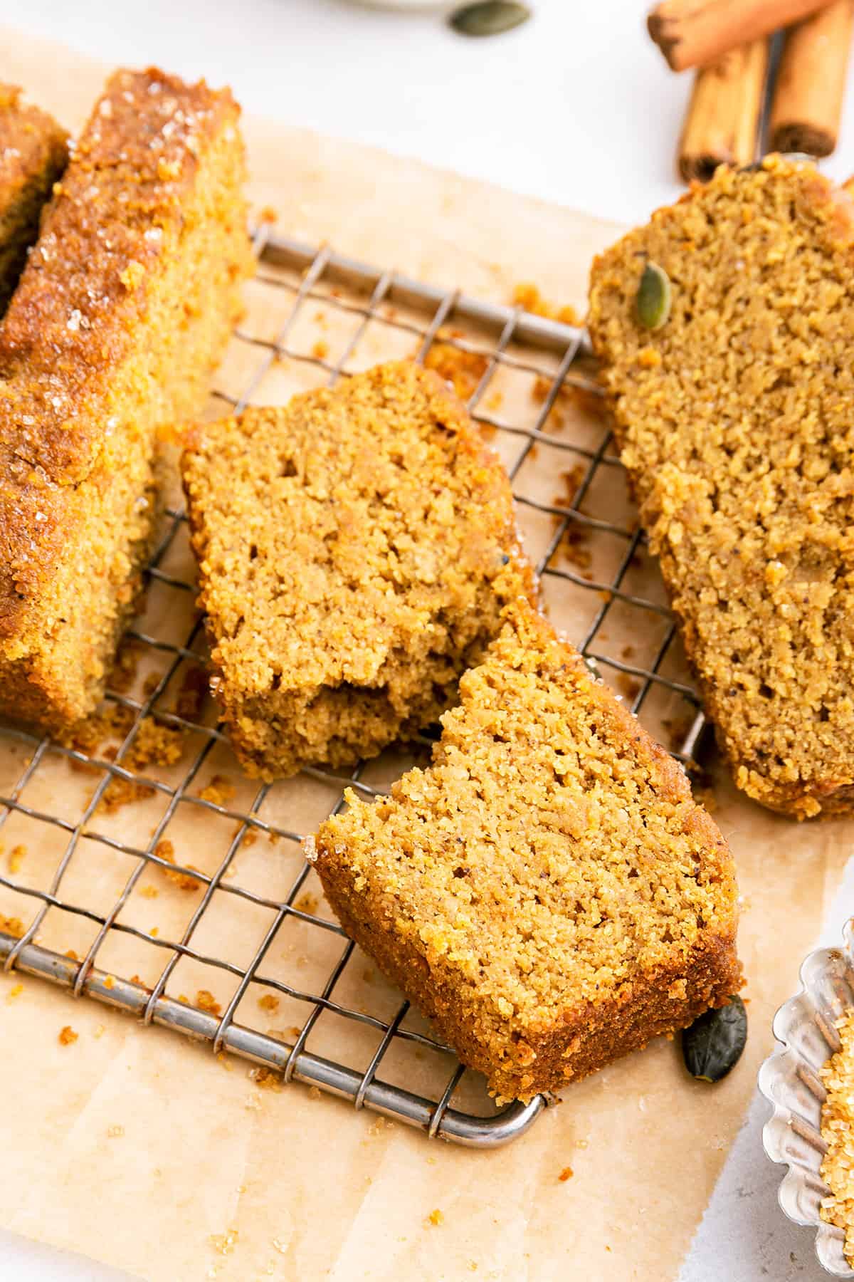 Slices of vegan pumpkin bread on wire rack set on cutting board, with one slice torn in half