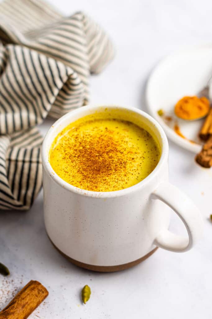 side view of a white mug with golden milk turmeric latte topped with cinnamon powder