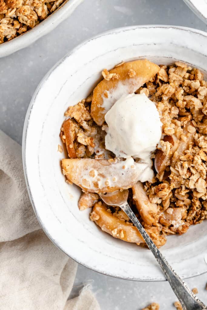 serving of vegan pear and apple crisp in a white ceramic bowl with ice cream