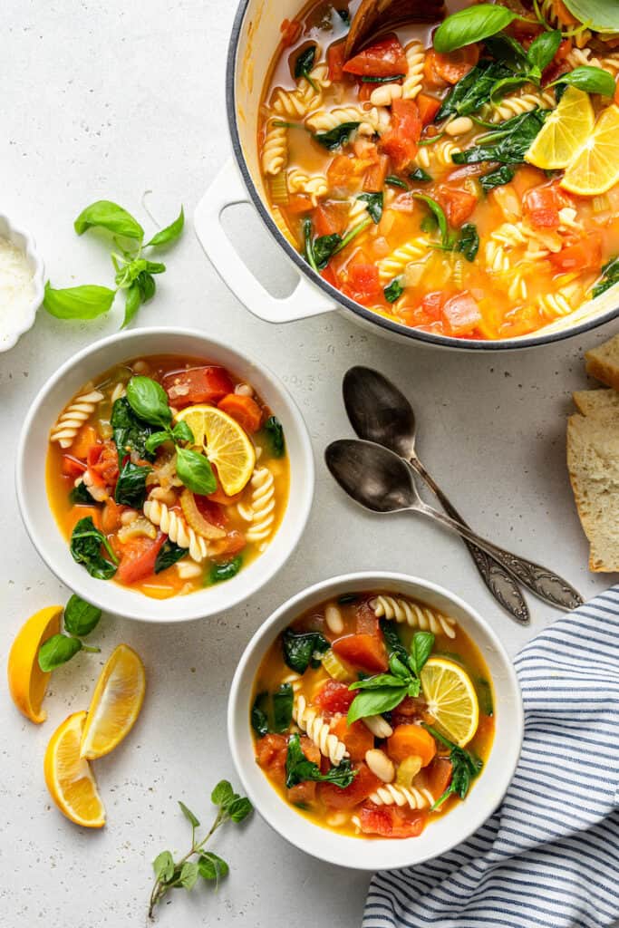 two bowls of vegetable and pasta soup with lemon and basil