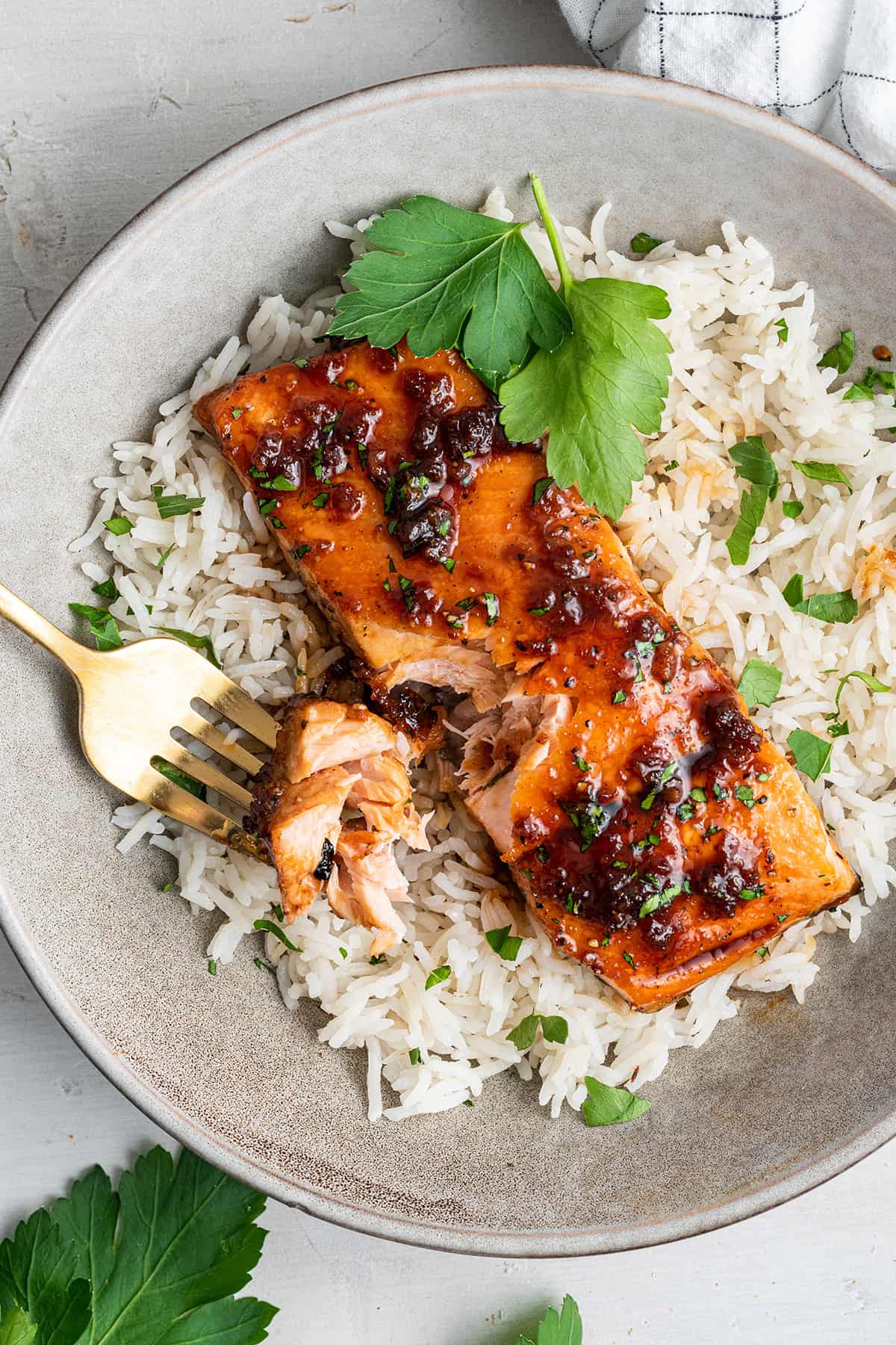 Overhead view of a honey glazed salmon filet on a bed of cilantro rise, with a fork holding a bite of salmon