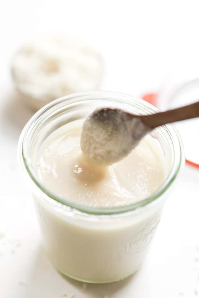 A jar of coconut butter with a wooden spoon being pulled out of it