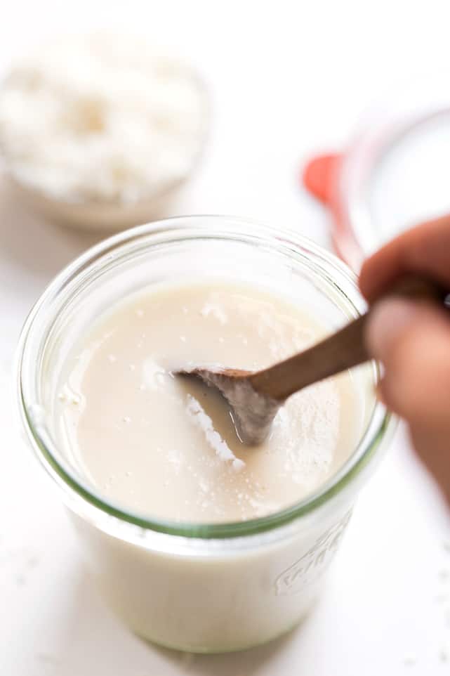A jar of coconut butter, with a hand holding a wooden spoon in it