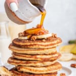 Pouring maple syrup onto stack of oatmeal banana pancakes