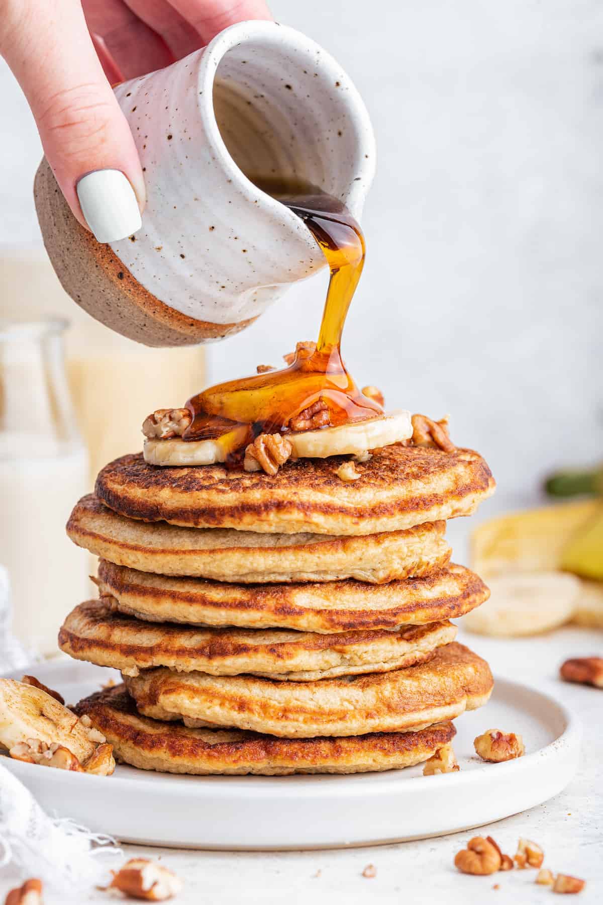 Pouring maple syrup onto stack of oatmeal banana pancakes