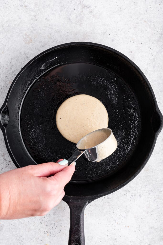 Overhead view of measuring cup pouring pancake batter into skillet