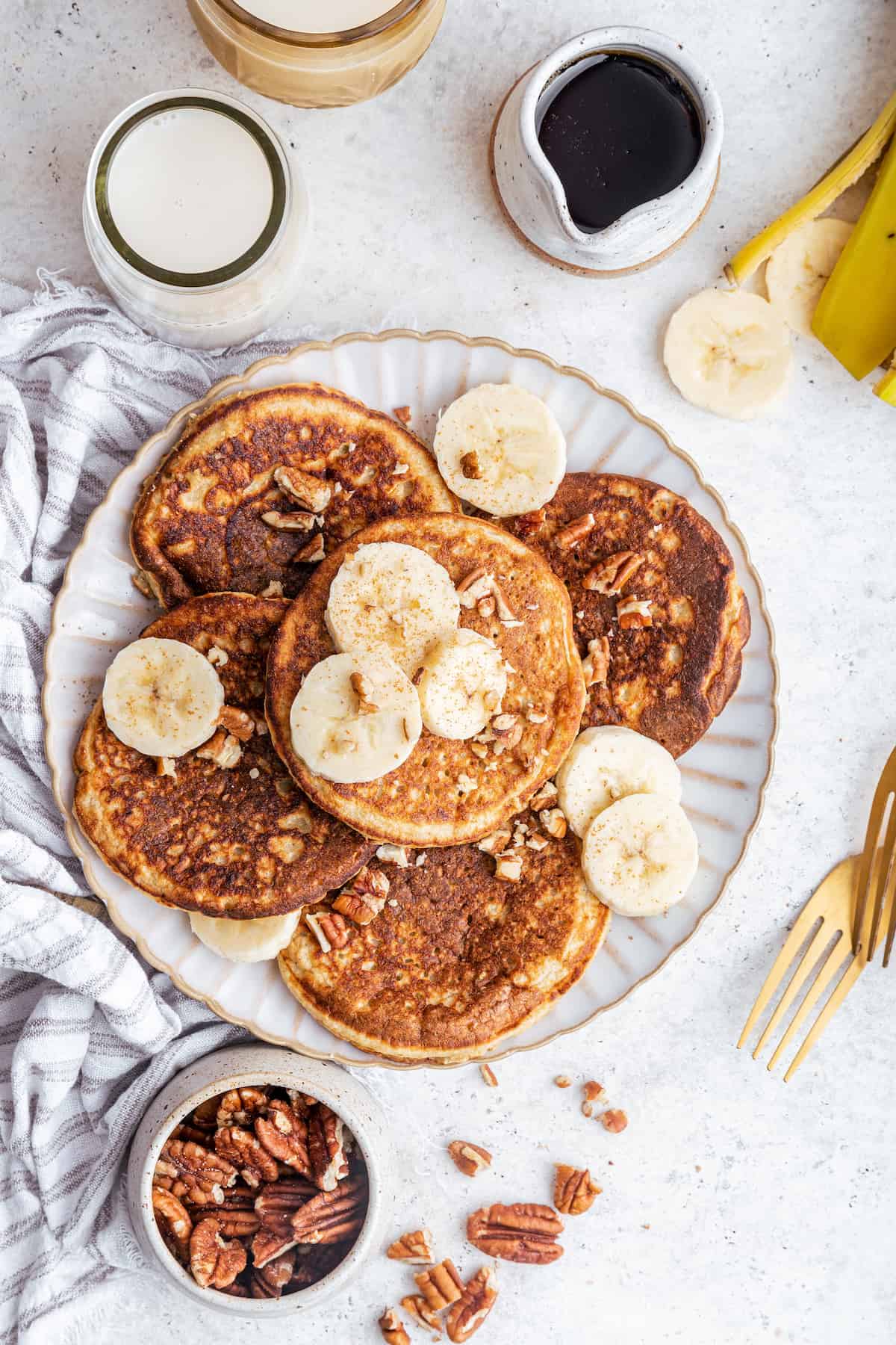 Overhead view of oatmeal banana pancakes on plate with pecans and bananas