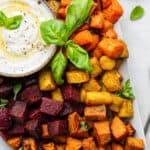 Overhead view of oven-roasted root vegetables on platter with bowl of yogurt dip