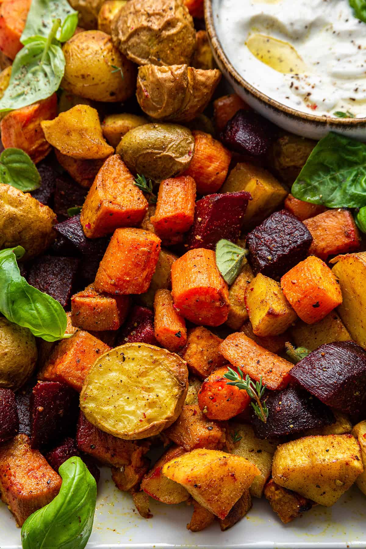 Overhead view of roasted root vegetables with bowl of yogurt dip