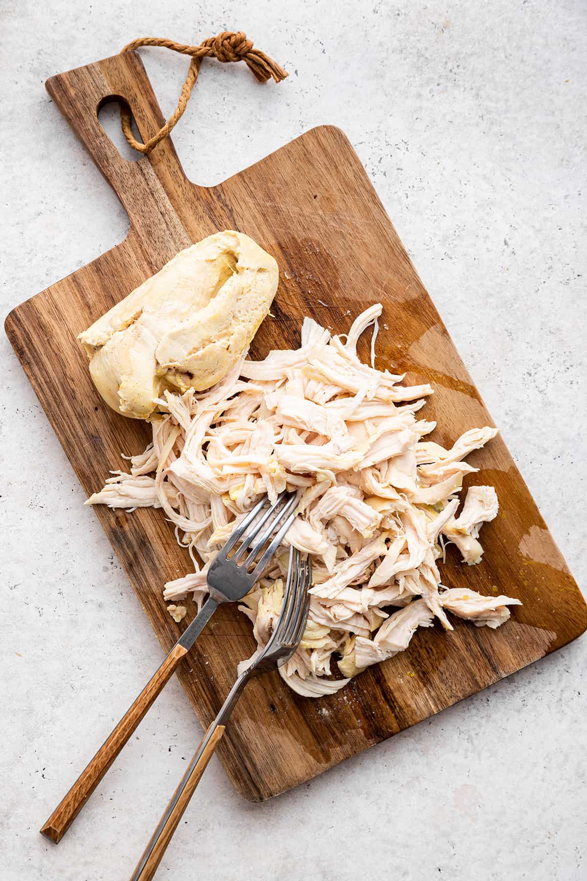 Overhead view of shredded chicken and forks on wood cutting board