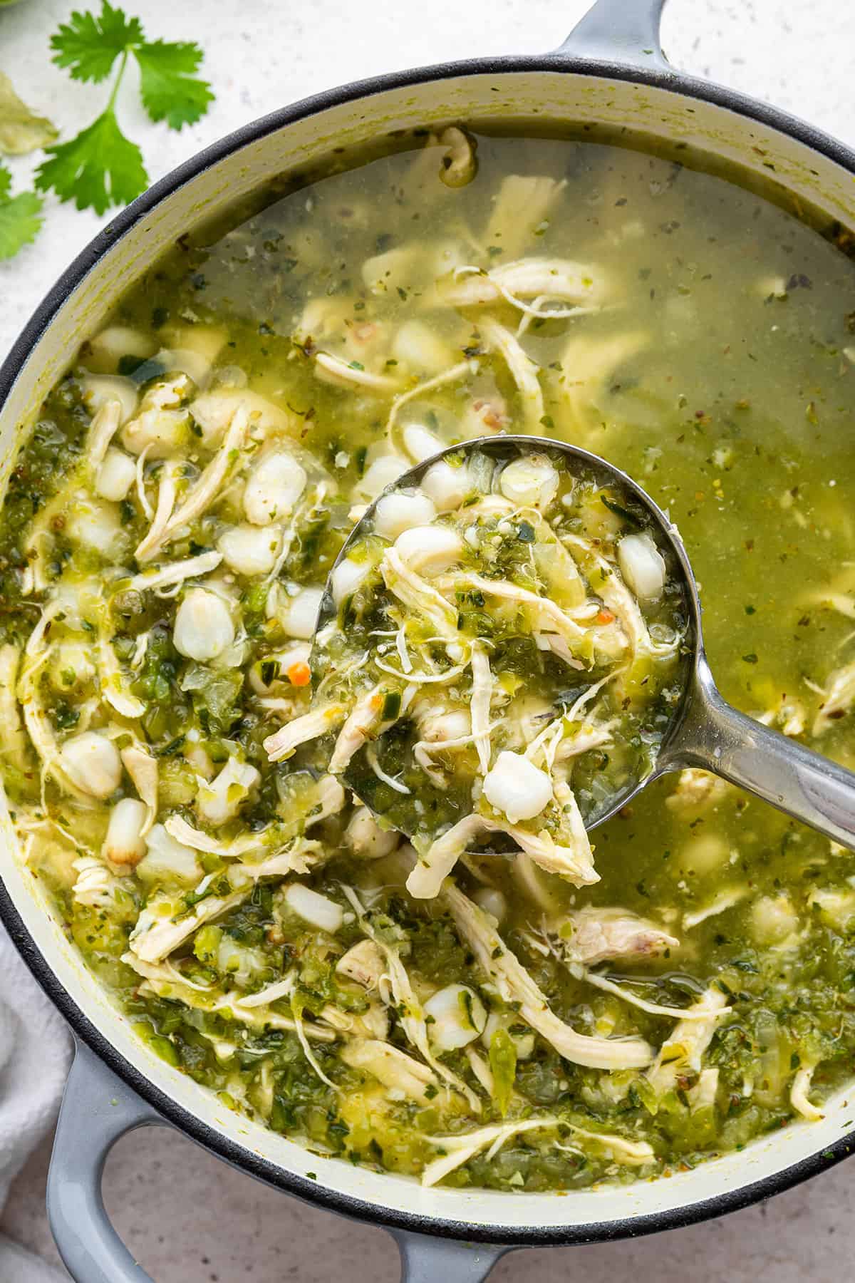 Cooked pozole verde in enamel cast iron Dutch oven with ladle