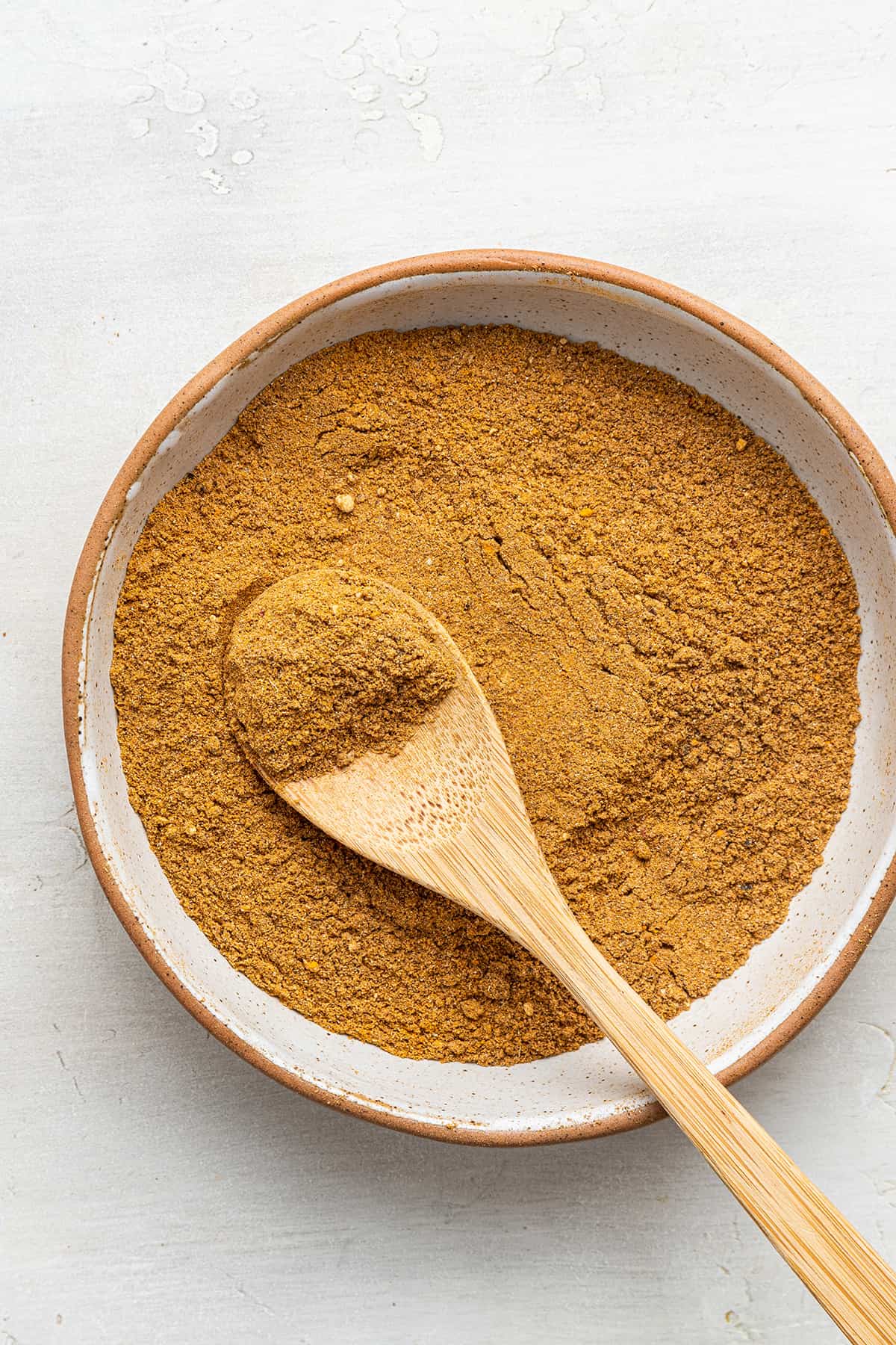 Overhead view of a wooden spoon in a bowl of ras el hanout