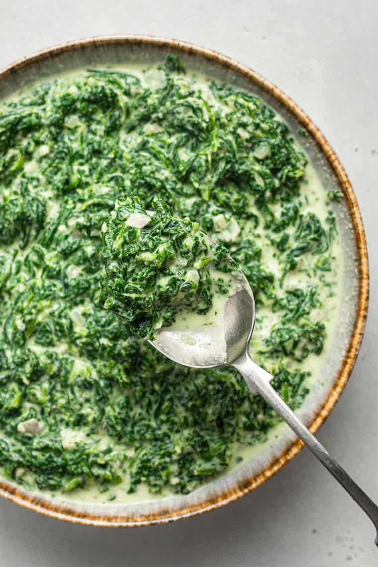 A bowl of creamed spinach with a spoon in it.