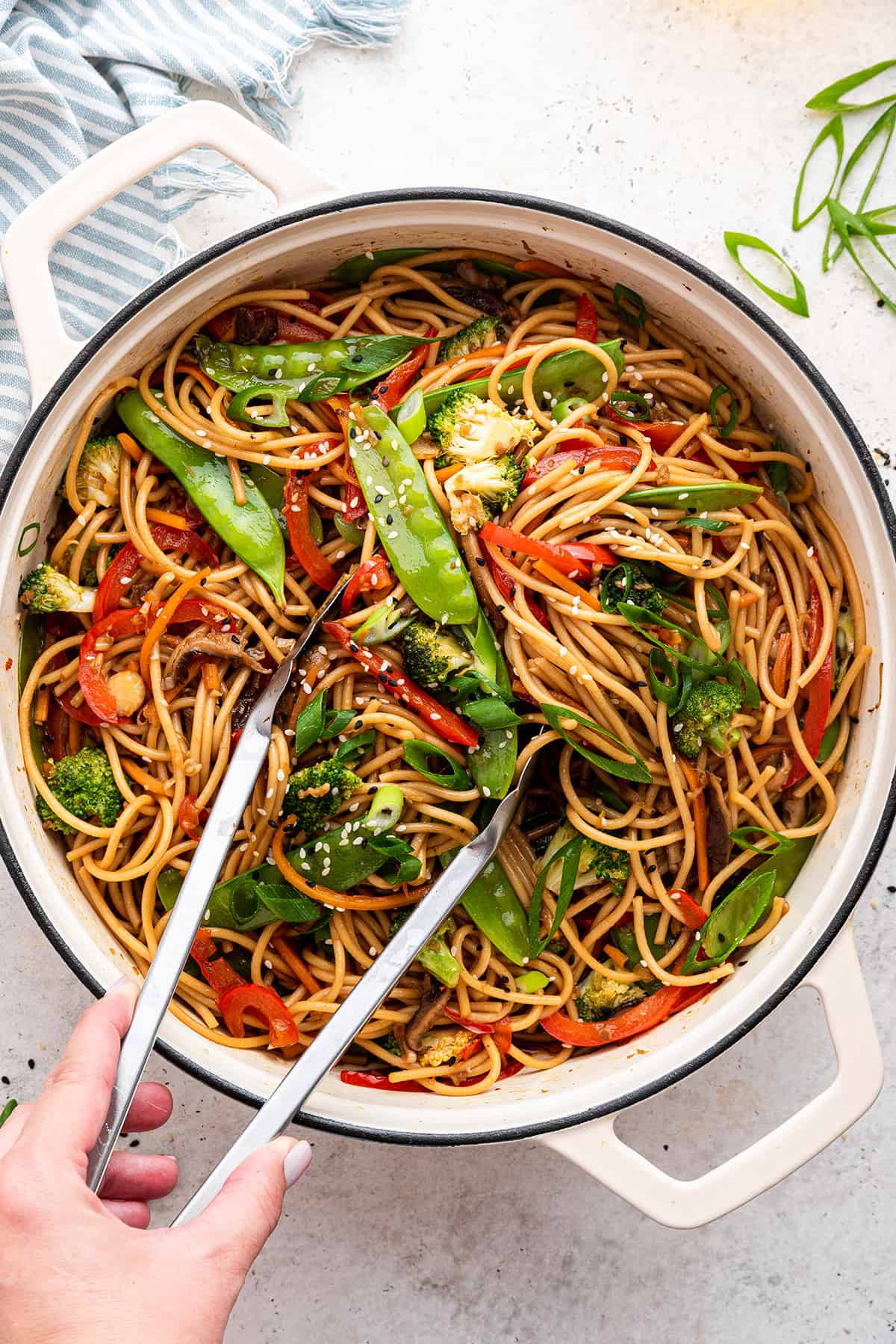 Hand reaching tongs into Dutch oven of vegetable lo mein