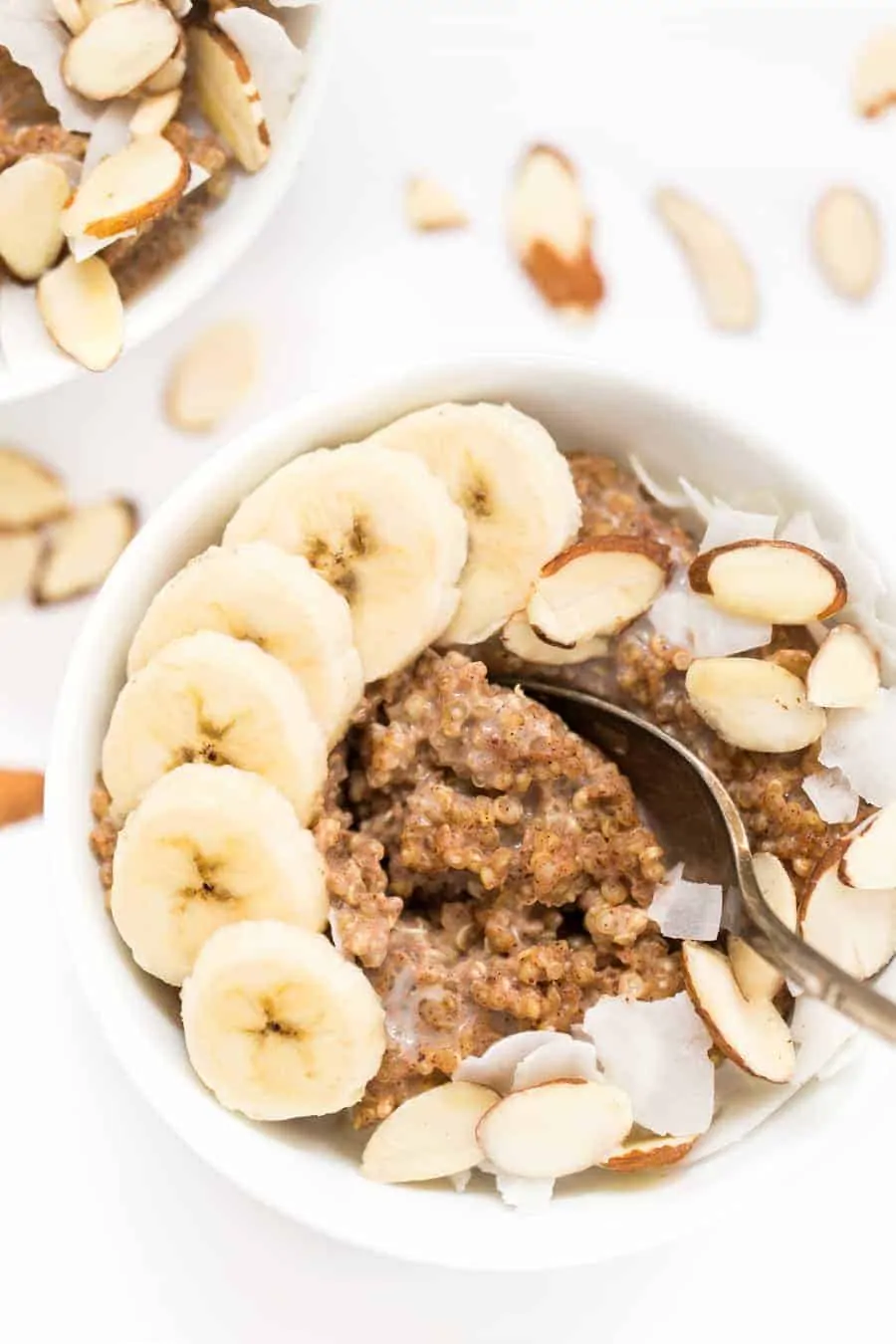 A bowl of breakfast quinoa topped with banana slices and slivered almonds, with a spoon in it