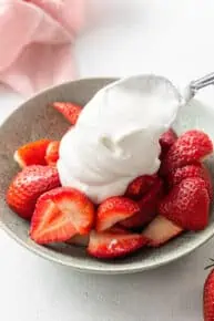 adding coconut whipped cream to strawberries