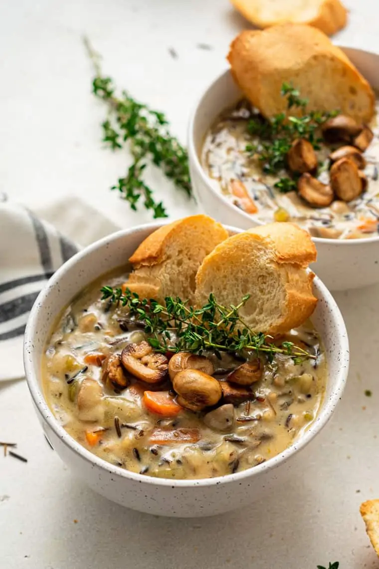 A bowl of wild rice soup topped with sautéd mushrooms, thyme sprigs, and slices of bread.