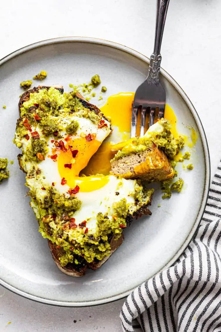fork taking a bite of pesto egg toast with a soft yolk