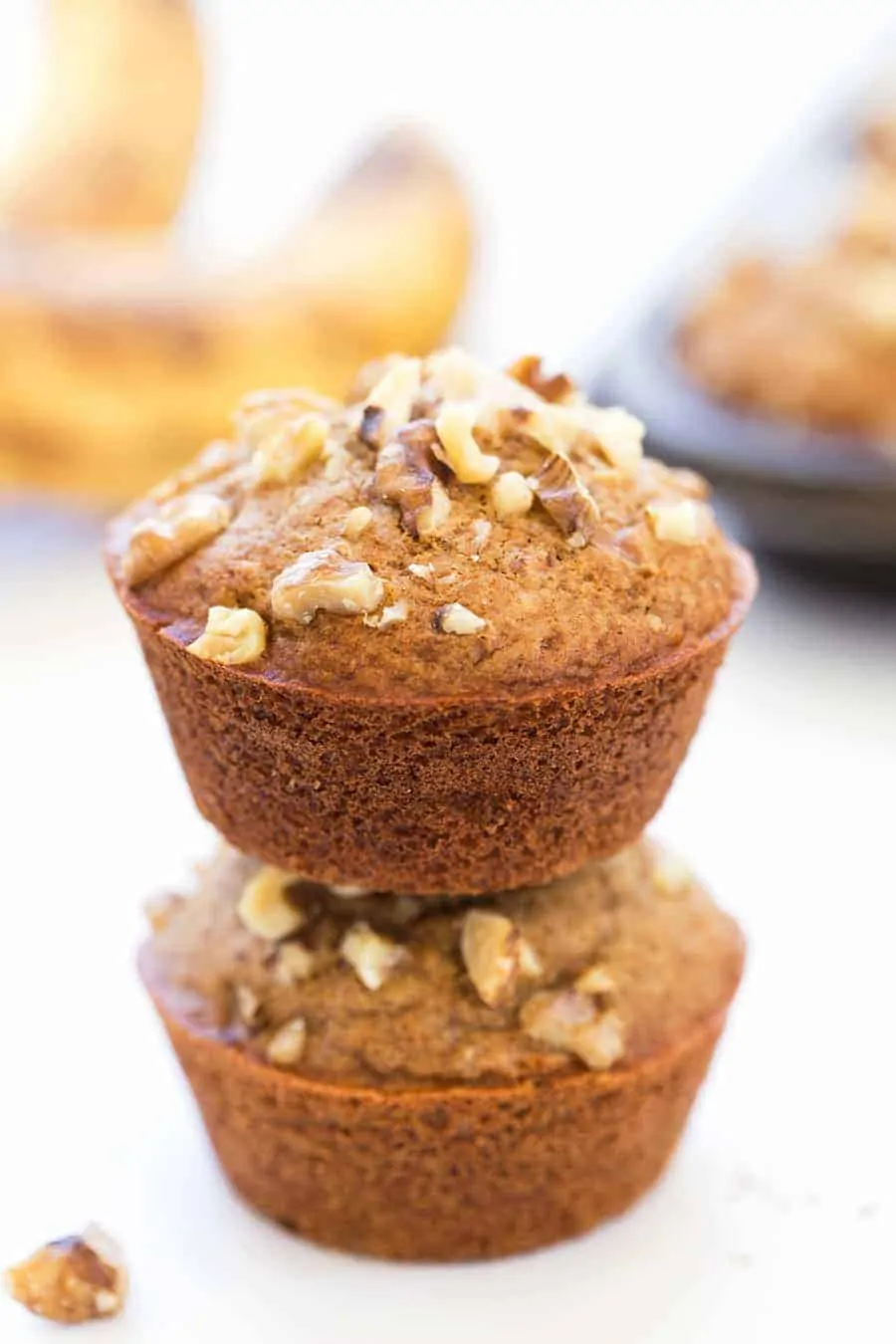 Two banana muffins stacked on top of each other, topped with walnuts. 