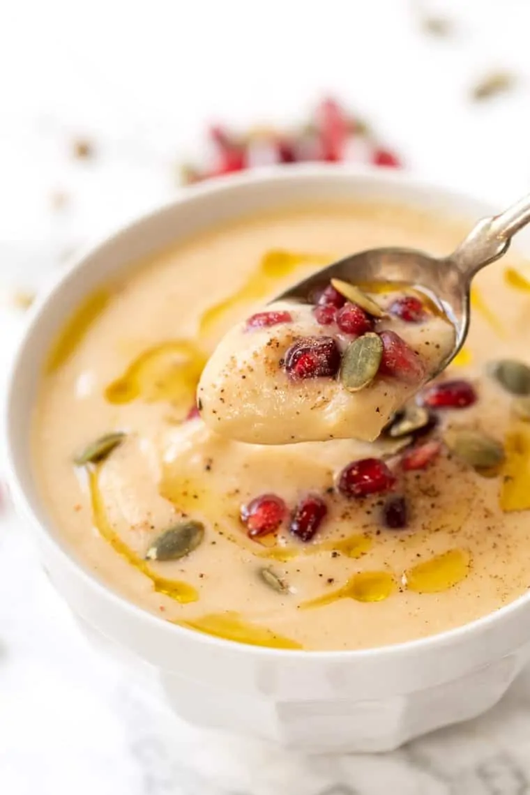 A spoon taking a spoonful of cauliflower soup out of a bowl