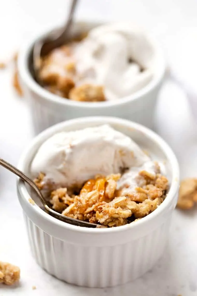 A bowl of peach crisp with ice cream, with a spoon in it.