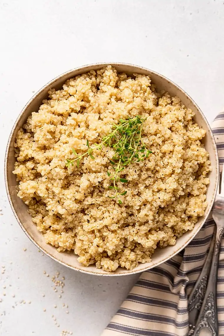 Overhead view of a bowl of quinoa topped with thyme and pepper, next to a napkin and a fork