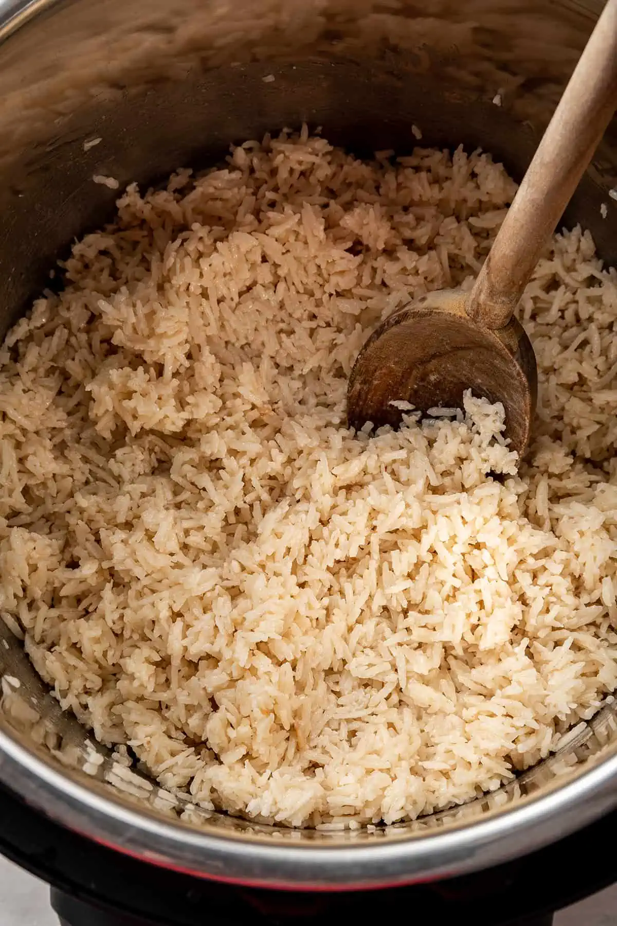 Coconut rice in an Instant Pot being fluffed with a wooden spoon.