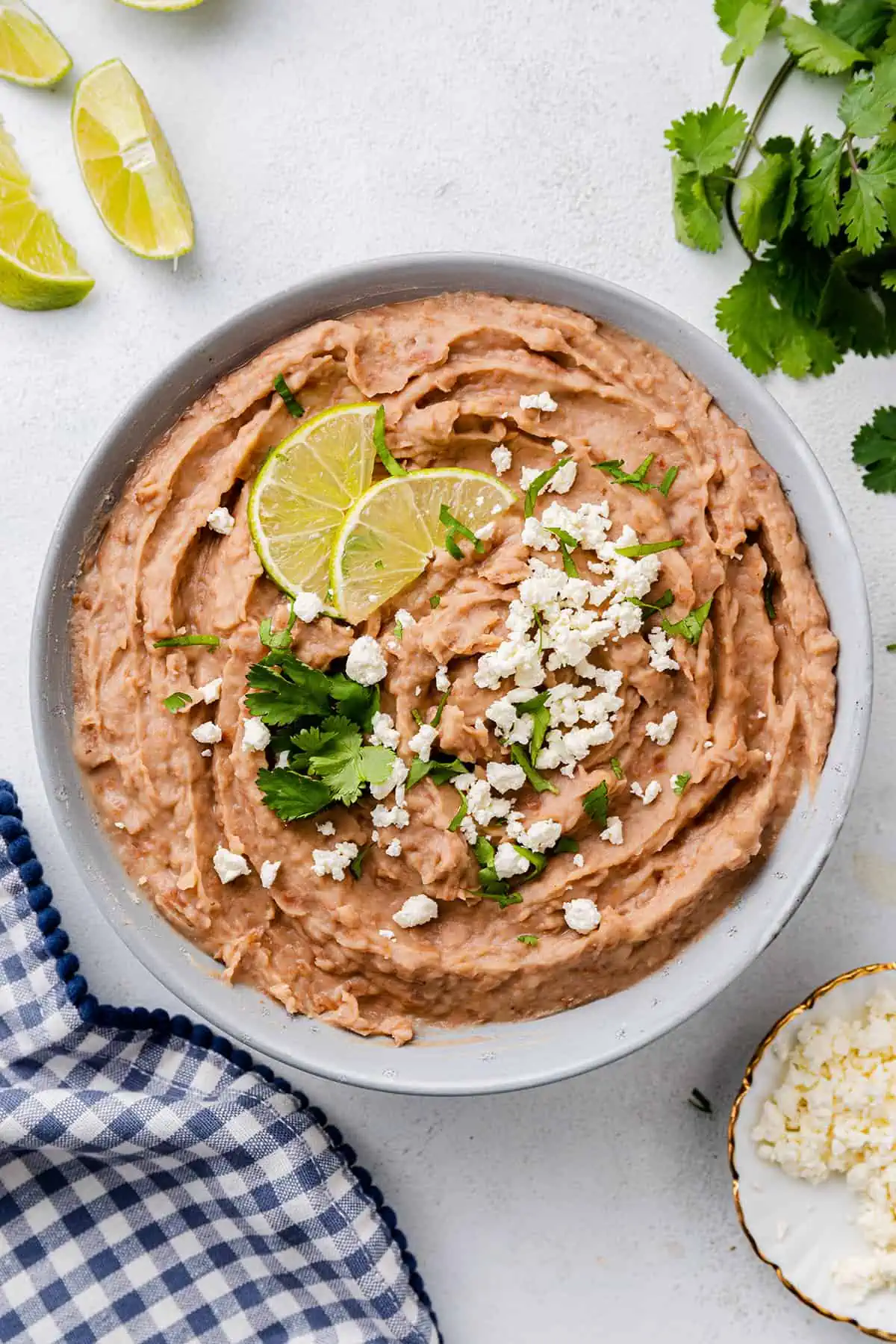 Overhead view of a bowl of refried beans topped with cheese, cilantro, and lime slices