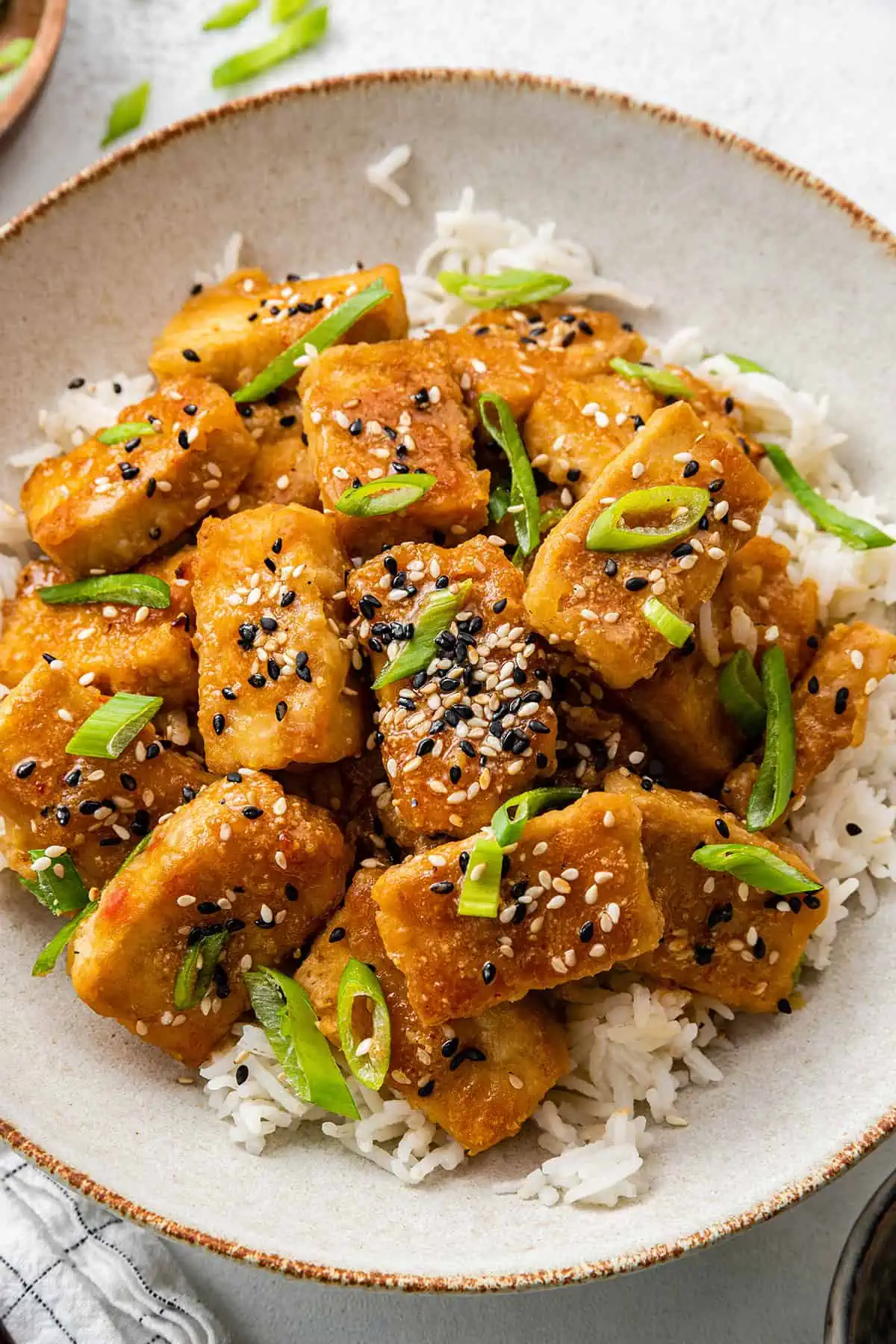 A pile of baked tofu on top of rice, topped with scallions and sesame seeds