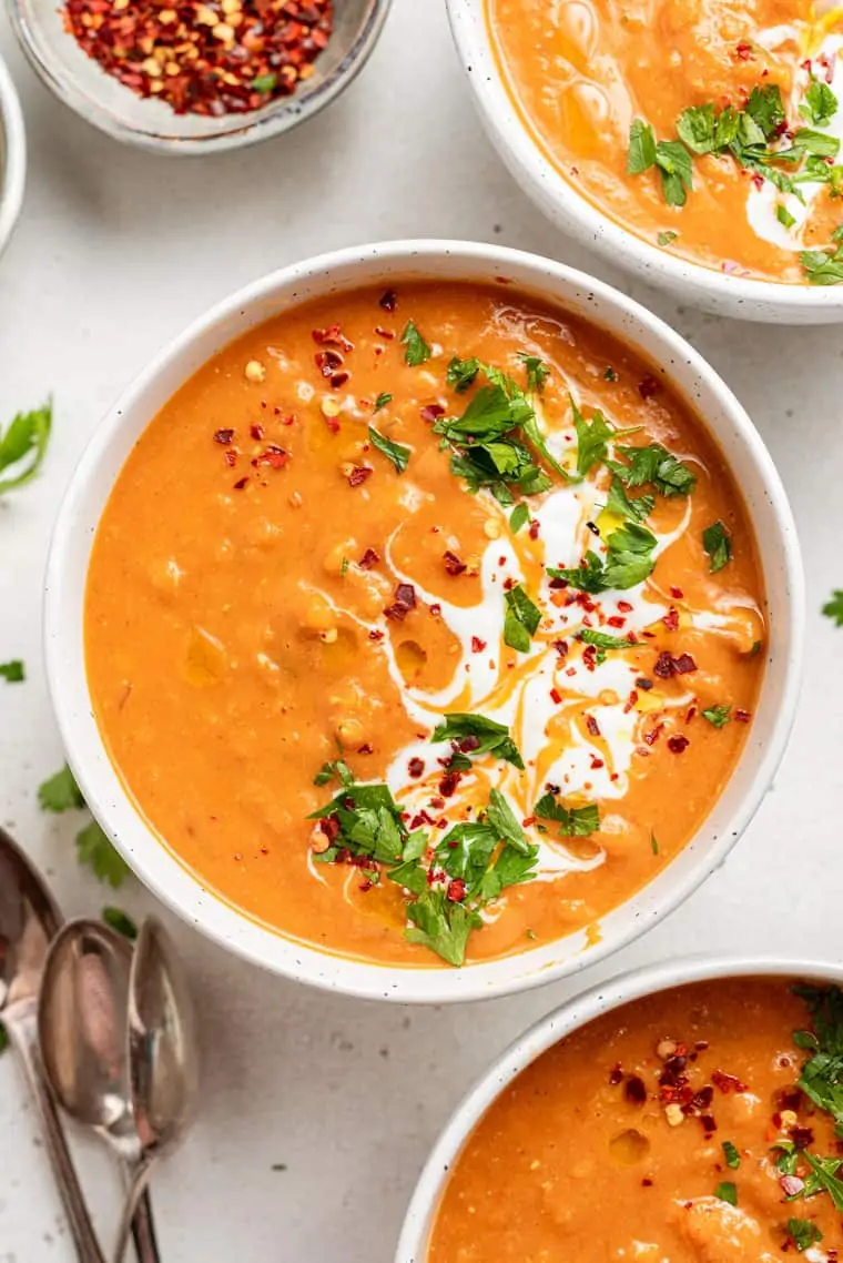 three bowls of red lentil soup with cream and herbs