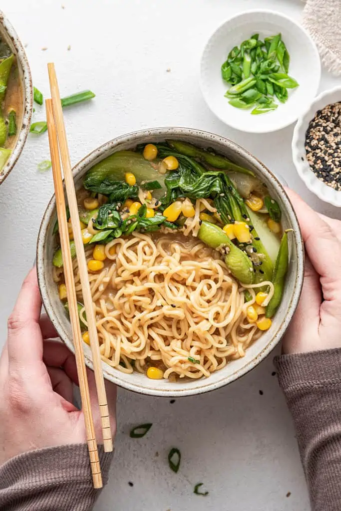 Overhead view of vegan ramen recipe with hands around bowl and chopsticks