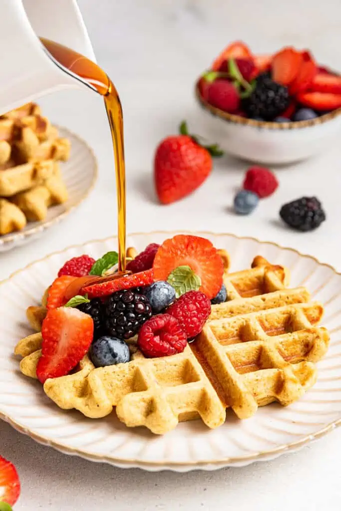 Pouring maple syrup on an almond flour waffle with berries
